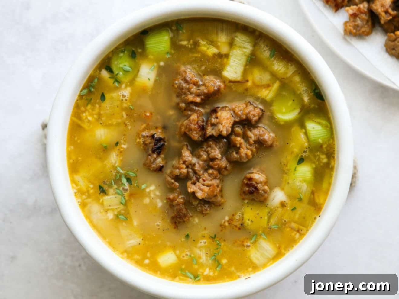 Cooked Italian sausage being returned to the simmering potato and leek soup, enhancing its heartiness and flavor.