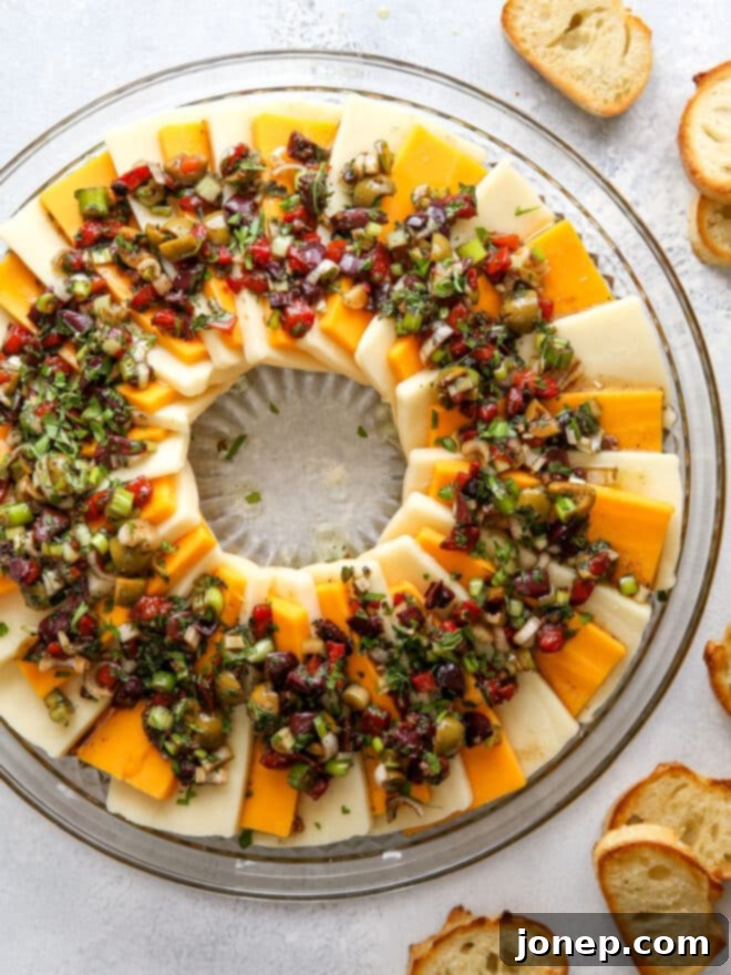 Zesty Marinated Cheese 2 Close-up of a festive marinated cheese wreath appetizer topped with olives and herbs, ready to be served.