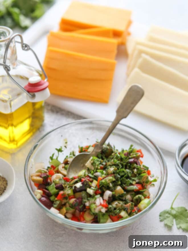 Zesty Marinated Cheese 4 Various chopped ingredients for the marinade topping, including olives, roasted red peppers, and green onions, in a mixing bowl.