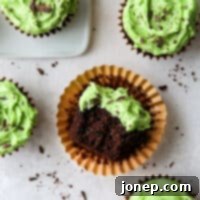 Minty Cocoa Bliss Cupcakes 11 A close-up of a mint chocolate chip cupcake with a bite taken out, showing its moist chocolate cake and creamy mint frosting.