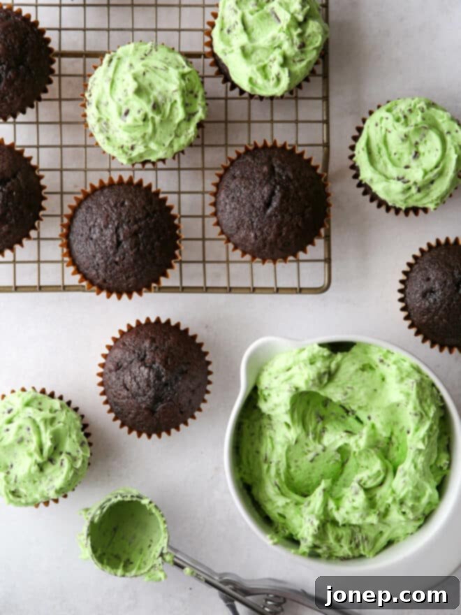 Hands meticulously frosting a rich chocolate cupcake with fluffy mint chocolate chip buttercream using an offset spatula, creating a charming, rustic swirled effect.
