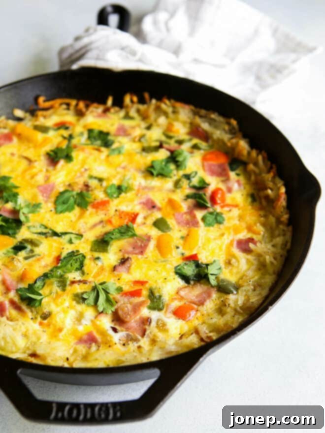 A slice of hash brown frittata with ham, peppers, and spinach on a white plate with a fork.