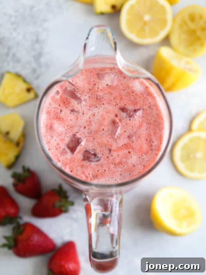 Close-up of Strawberry Pineapple Punch in a glass pitcher with fresh fruit garnishes