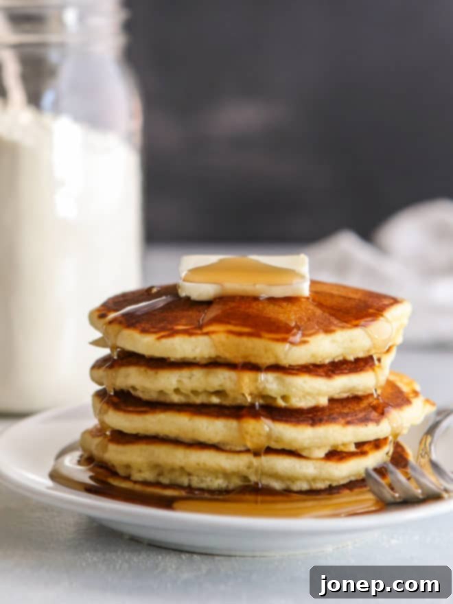 stack of fluffy pancakes on a plate garnished with fresh berries and drizzled with maple syrup