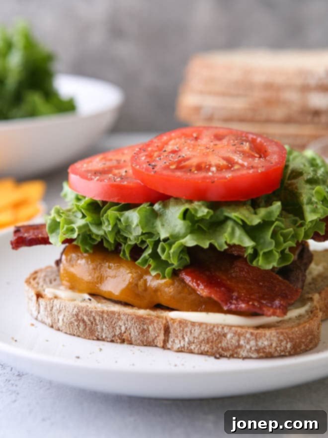 Cheeseburger topped with bacon, lettuce, and tomato served on toasted white bread