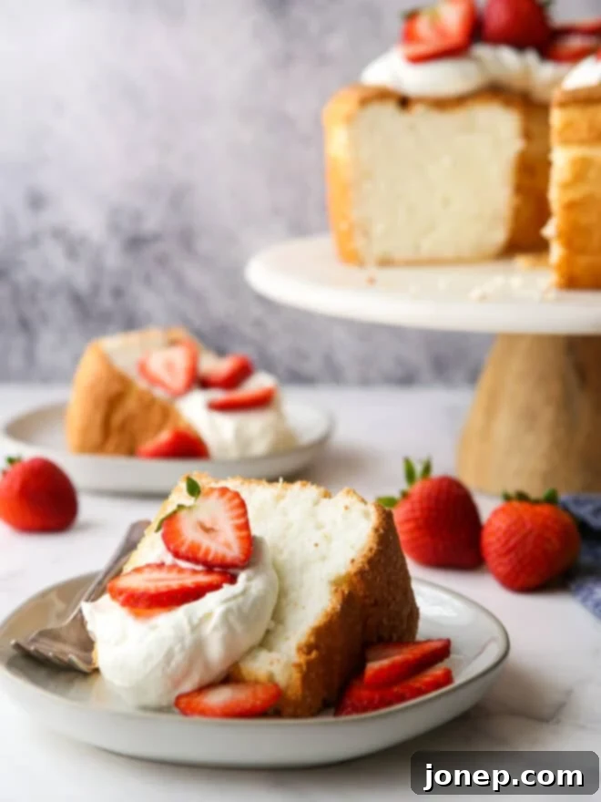 A close-up of a slice of angel food cake on a white plate, topped with whipped cream and fresh strawberries, inviting to be eaten.