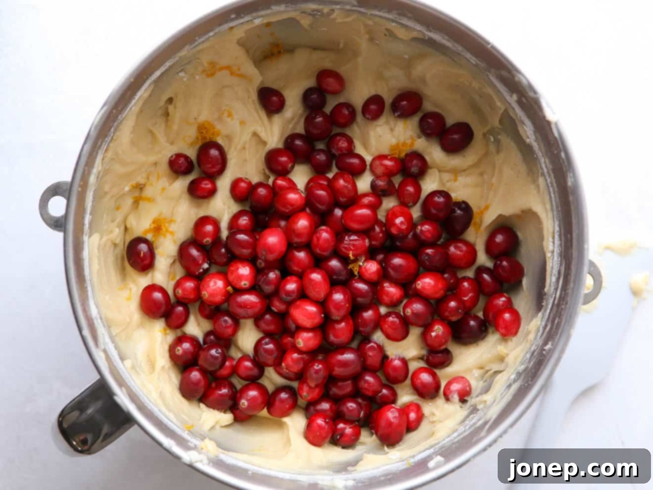 Fresh cranberries being gently folded into the bundt cake batter by hand.