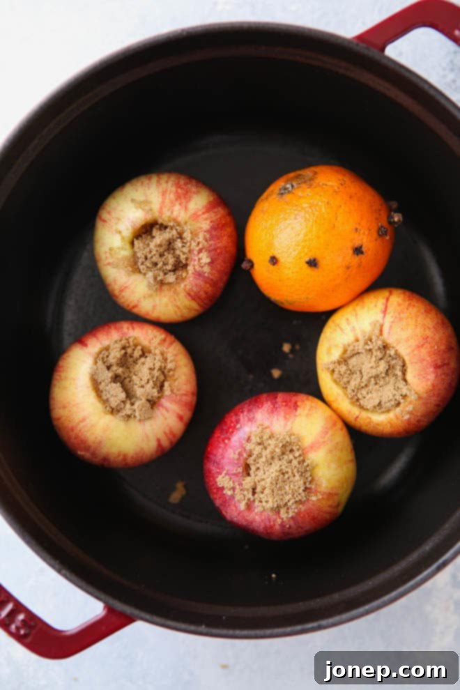 Close-up of baked apples, orange, and spices steeping in hot wassail in a pot on the stove.