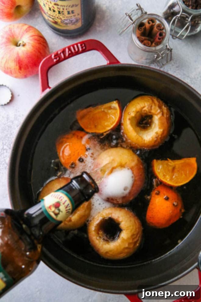 Overhead view of hot wassail simmering in a Dutch oven, featuring baked apples, orange slices, and whole spices.