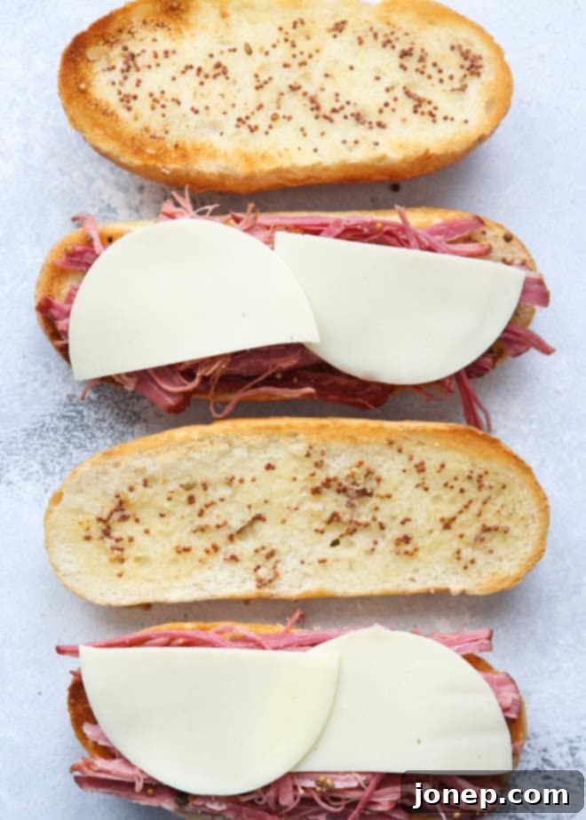 Assembling corned beef french dip sandwiches with layers of beef, sauerkraut, and cheese