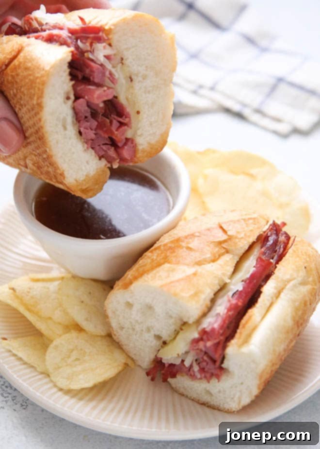 A person dipping a corned beef french dip sandwich in a small bowl of au jus