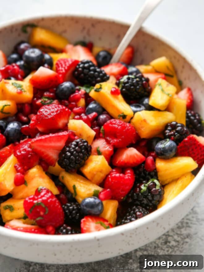 Luscious Berry Fruit Salad 5 Closeup of a colorful fruit salad with berries, pineapple, and pomegranate, showing the fresh mint leaves and a serving spoon.
