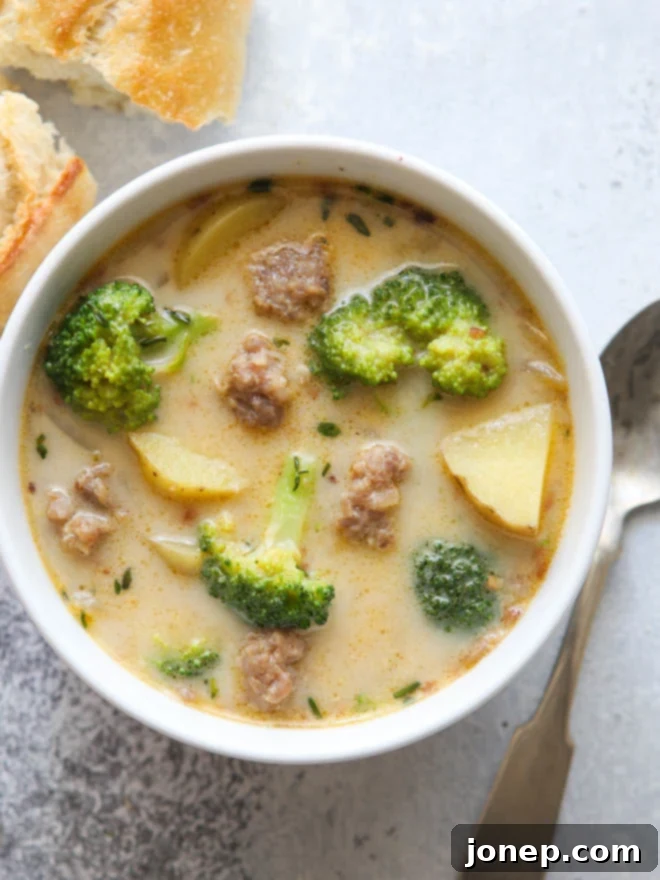 A bowl of hearty sausage, broccoli, and potato soup, garnished with fresh herbs.