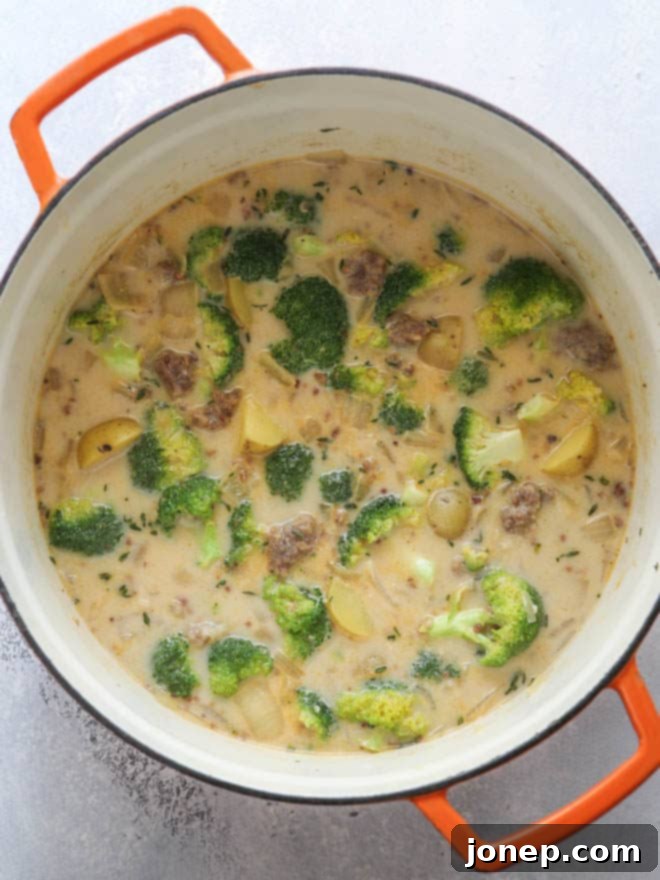 A pot of hearty sausage, broccoli and potato soup simmering on the stove, ready to be served.