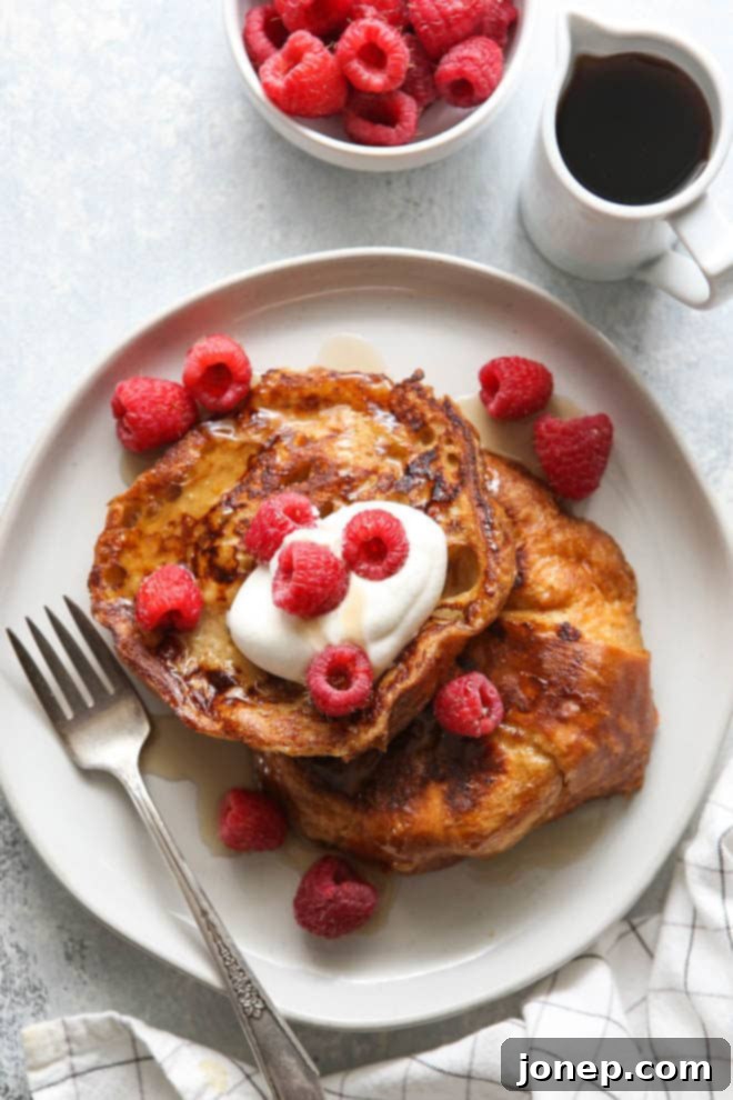 Platter of golden brown croissant French toast topped with whipped cream, fresh berries, and a drizzle of maple syrup