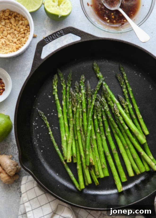 Close-up of vibrant green sautéed asparagus spears with a glossy ginger-lime sauce and scattered peanuts.