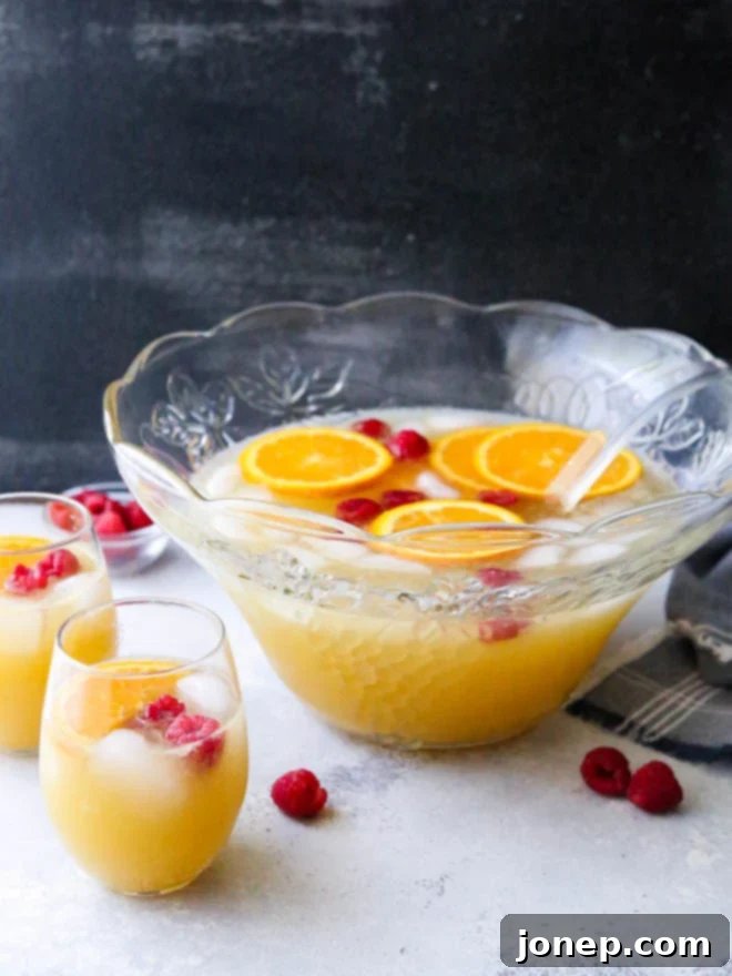 A vibrant Mimosa Punch served in a large glass punch bowl, garnished with orange slices and fresh raspberries, perfect for a brunch party.