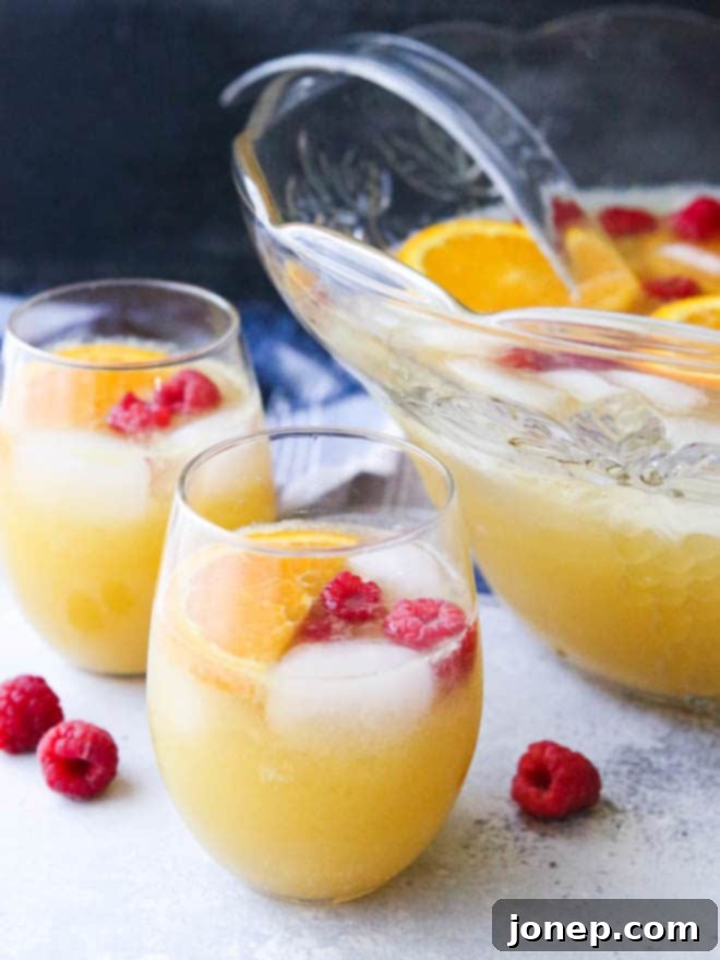 A refreshing Mimosa Punch with a focus on floating orange slices and bright red raspberries in a punch bowl, ready for a spring or summer brunch.