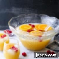 Sparkling Sunrise Punch 5 A festive Mimosa Punch with orange slices and raspberries in a punch bowl.