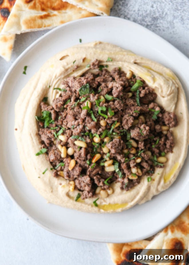 Creamy hummus topped with richly spiced ground beef, golden pine nuts, and fresh parsley and mint, served with warm pita bread – an ideal appetizer or light meal for any occasion.