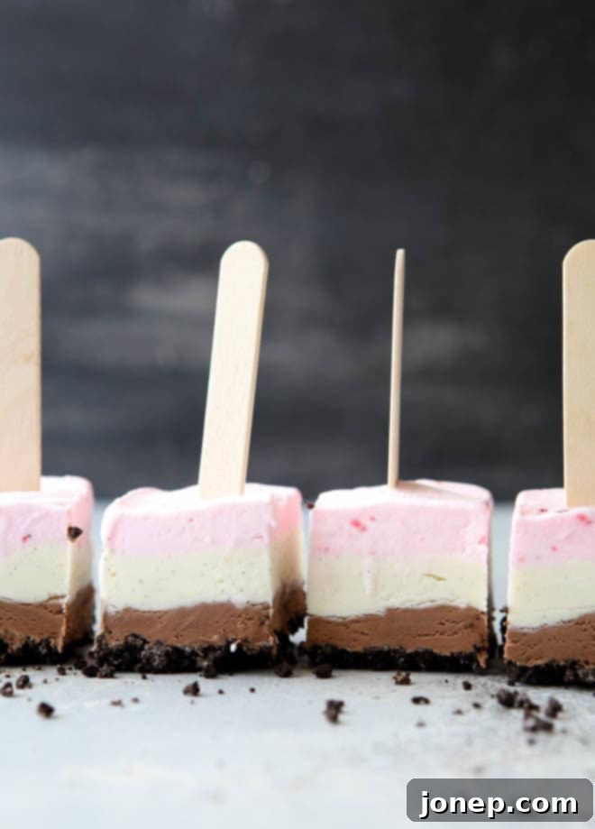A stack of freshly made Neapolitan ice cream pops, showing the beautiful distinct layers of Oreo crust, chocolate, vanilla, and strawberry ice cream, ready to be wrapped and stored or served.