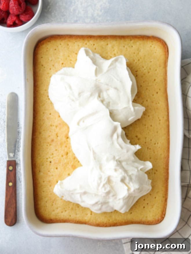 The three-milk mixture being carefully poured over the entire surface of the poked Tres Leches cake, illustrating the soaking process.