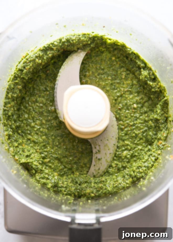 Partially blended basil walnut pesto in a food processor, demonstrating the chunky stage before adding more olive oil.