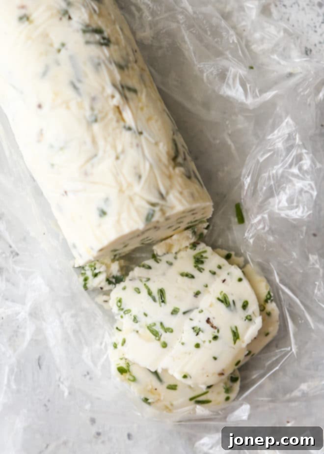 A close-up shot of freshly made chive compound butter, bright green with chopped chives, shaped into a log on plastic wrap, ready for chilling.