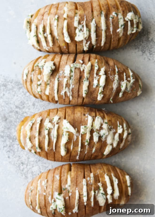 Hasselback potatoes with thin slices of chive butter nestled into the cuts, ready to be wrapped for grilling.
