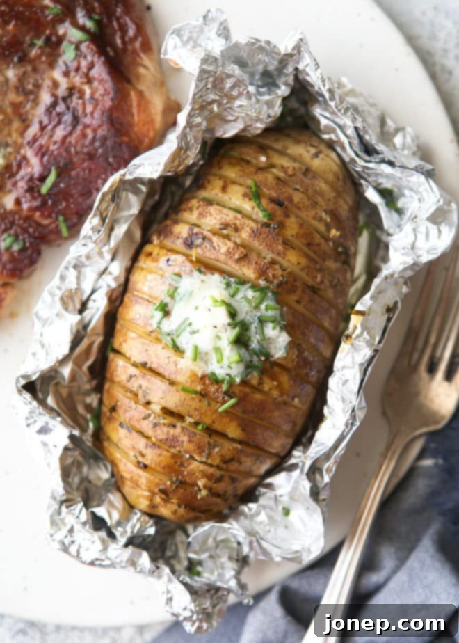 A plate of two grilled hasselback potatoes, golden brown and fanned open, topped with melting chive butter and fresh chives.