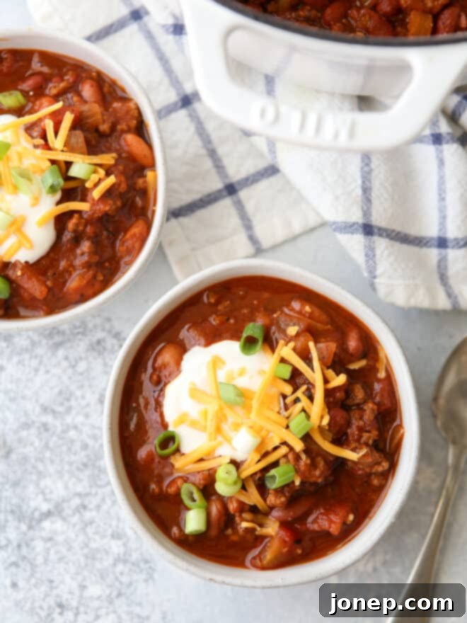 Effortless Weeknight Chili 2 Hearty bowls of easy weeknight chili with a spoon, topped with cheese and green onions