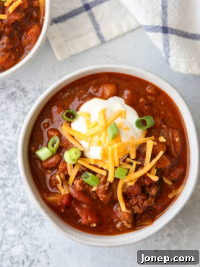 Effortless Weeknight Chili 7 Closeup of a single bowl of hearty chili, richly garnished with sour cream, shredded cheese, and fresh green onions