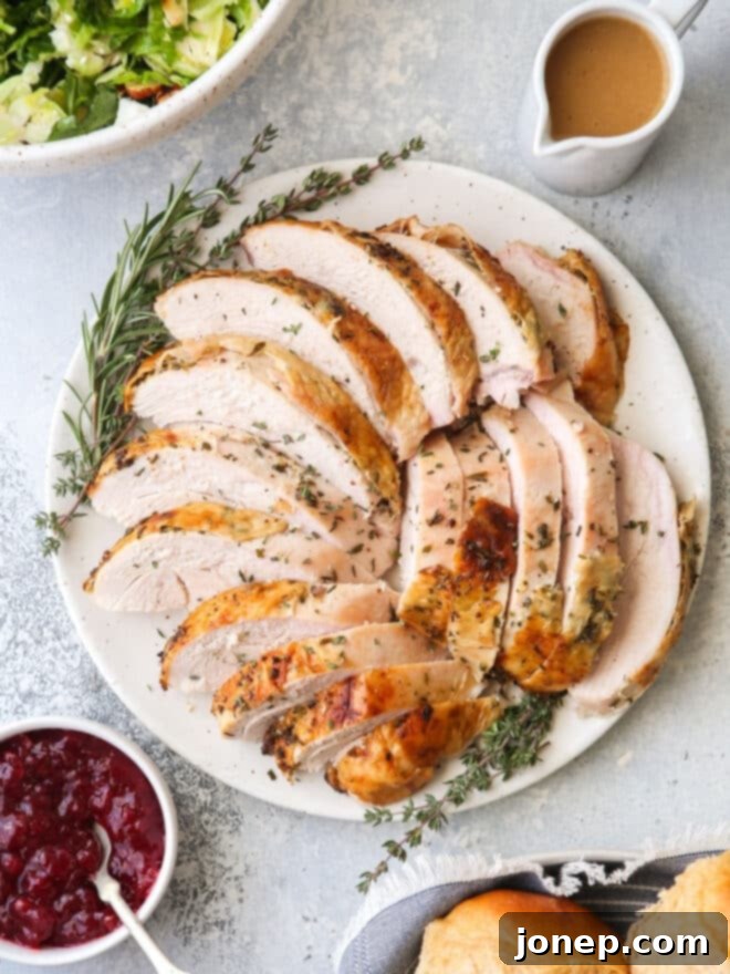 Aromatic Herb-Roasted Turkey Breast 15 sliced roasted turkey on a platter alongside a salad, cranberry sauce, gravy and rolls, ready to serve