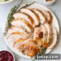 Aromatic Herb-Roasted Turkey Breast 7 sliced roasted turkey on a platter alongside a salad, cranberry sauce, gravy and rolls, ready for a holiday meal