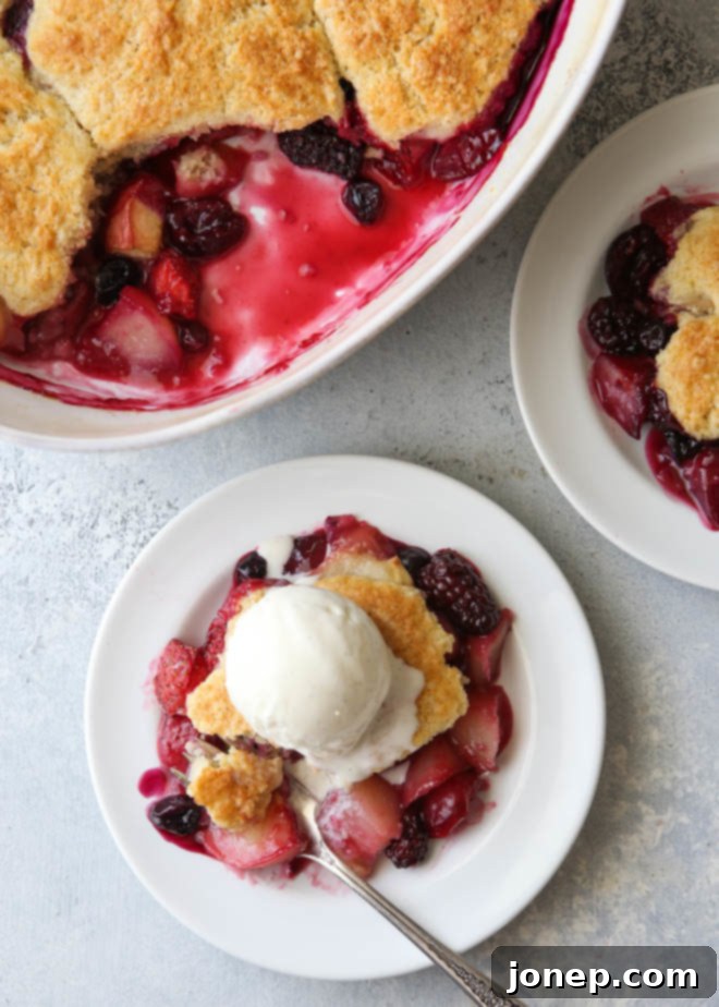 A vibrant, baked summer fruit cobbler, showcasing a mix of peaches, plums, cherries, and berries under a golden-brown, cake-like topping.