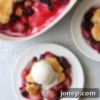 A vibrant, baked summer fruit cobbler, showcasing a mix of peaches, plums, cherries, and berries under a golden-brown, cake-like topping.