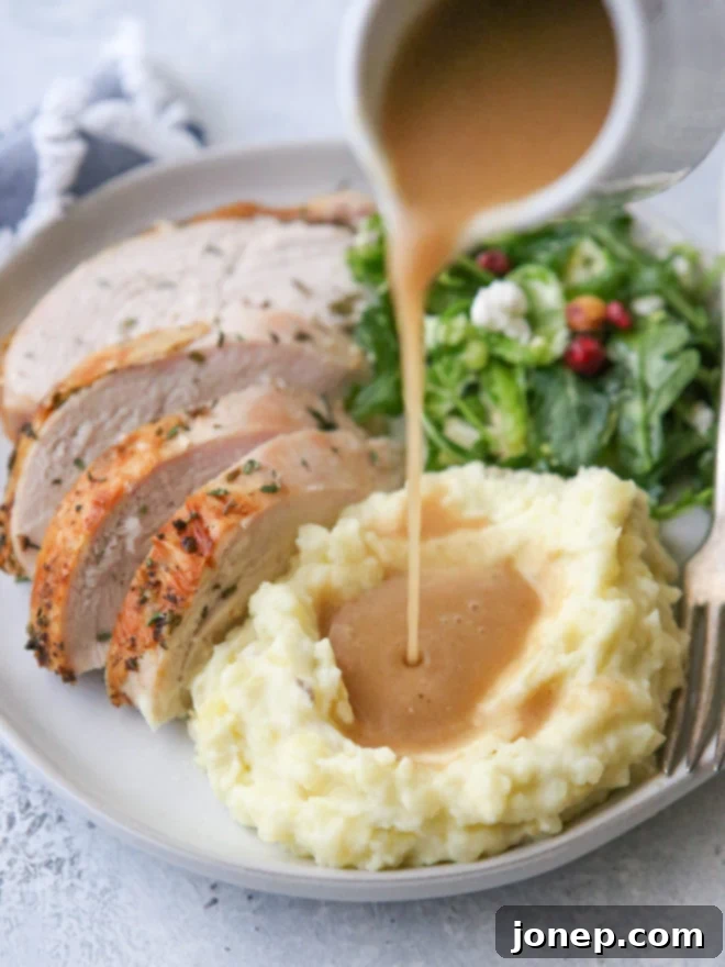 Perfect Homemade Turkey Gravy 2 Close-up of golden homemade turkey gravy, made from pan drippings, poured over mashed potatoes on a Thanksgiving plate.