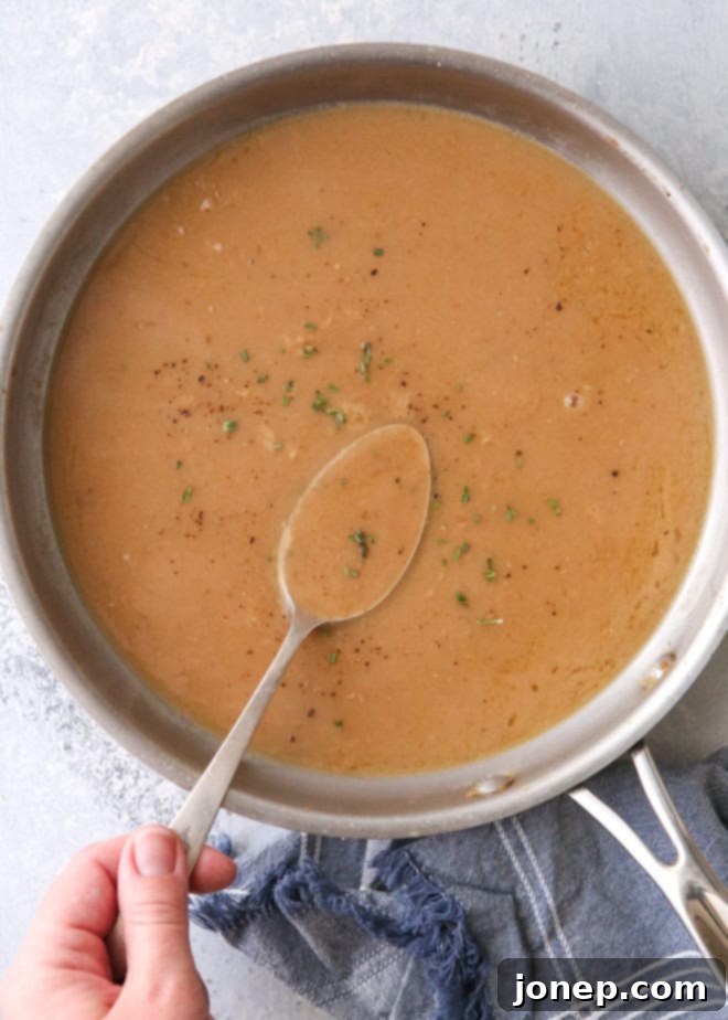 Perfect Homemade Turkey Gravy 4 A close-up of turkey gravy simmering in a saucepan, being whisked to a smooth consistency.