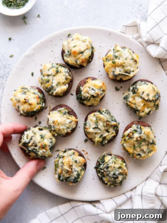 a hand grabbing a spinach artichoke stuffed mushroom