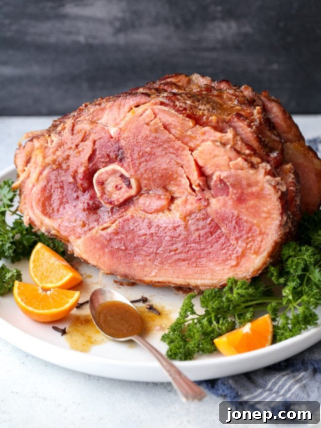 A beautifully presented Citrus Spice Glazed Ham, garnished with fresh orange slices and herbs, ready to be served as a main dish for a gathering.
