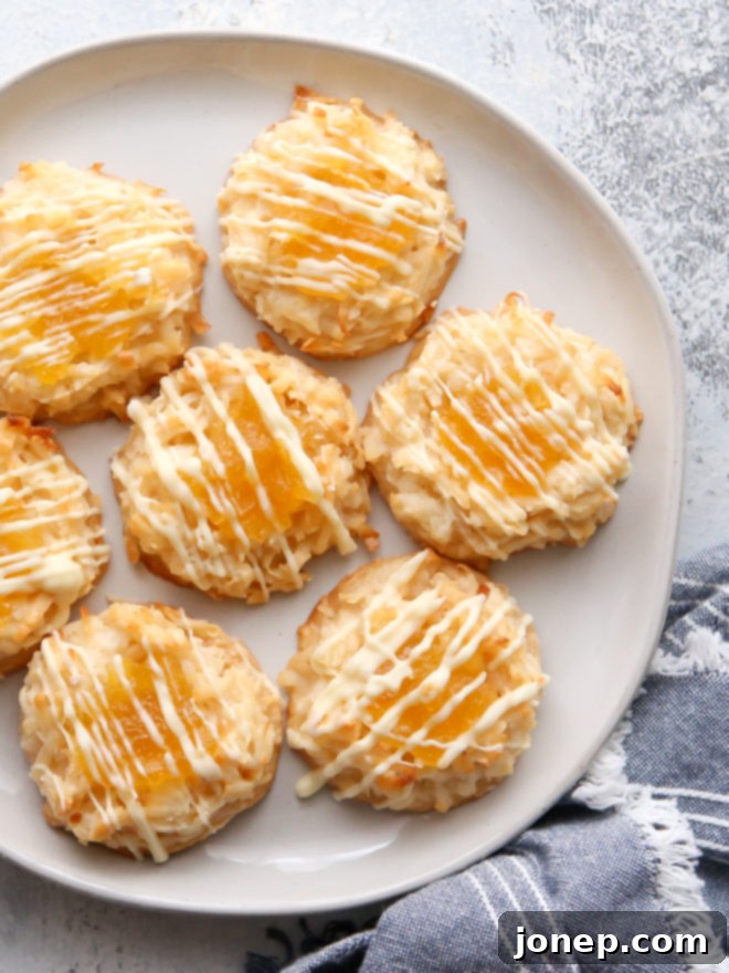 Delicious, golden-brown pineapple coconut macaroons with a bright pineapple jam center and white chocolate drizzle on a baking sheet, ready to be enjoyed.