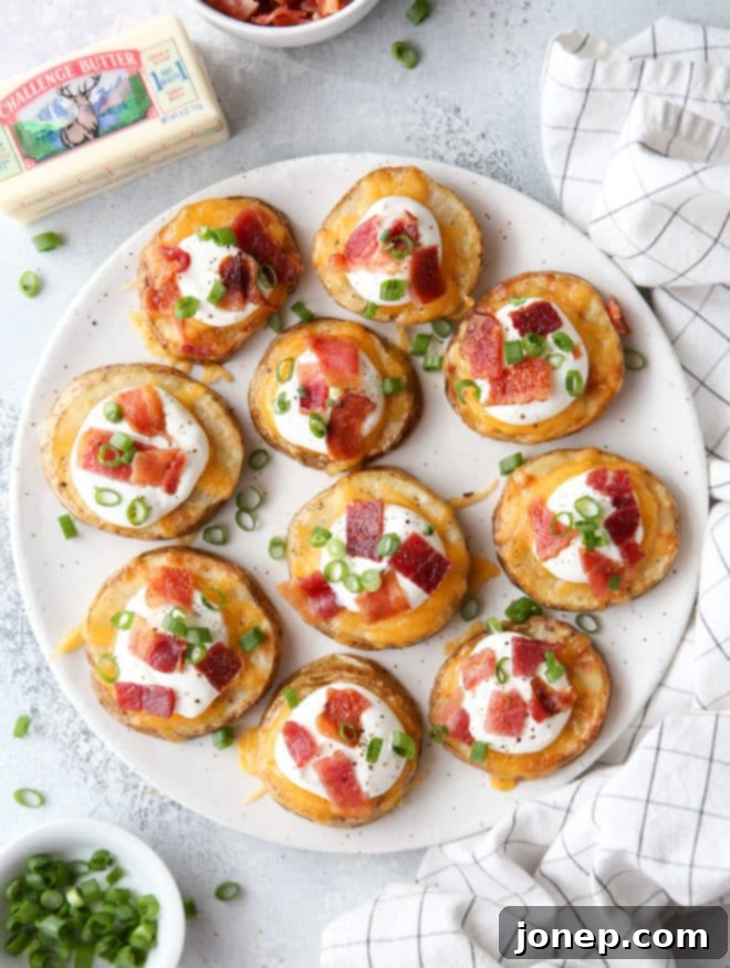 A close-up shot of a platter of finished loaded baked potato bites, generously topped with melted cheddar cheese, sour cream, crispy bacon crumbles, and fresh green onions, ready to be served.