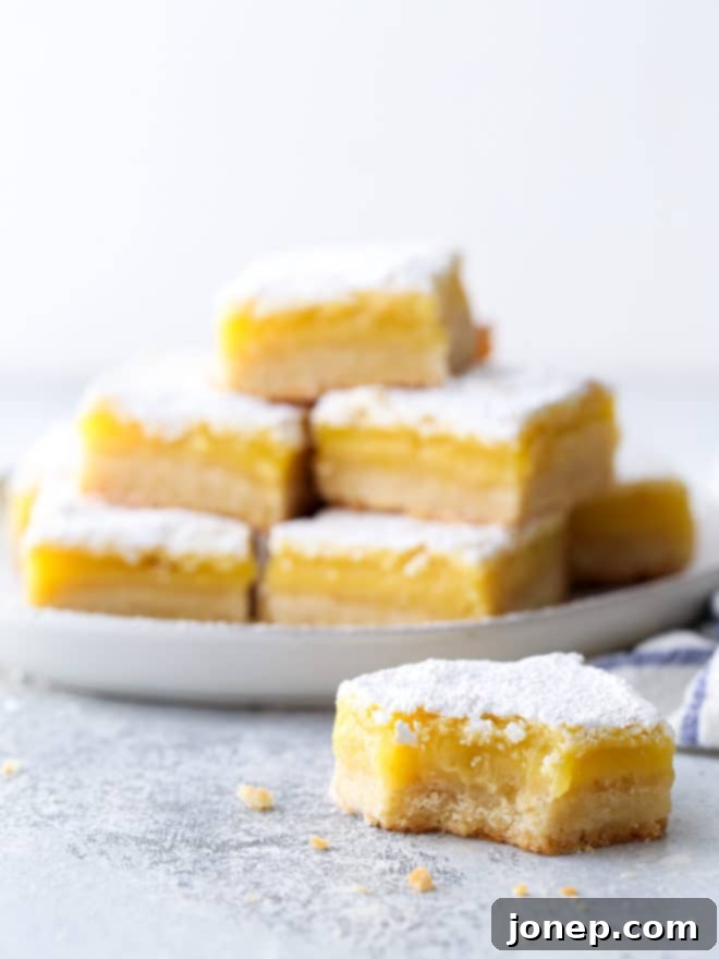 A tray of freshly baked lemon bars, some sliced and others whole, glistening under a layer of powdered sugar.
