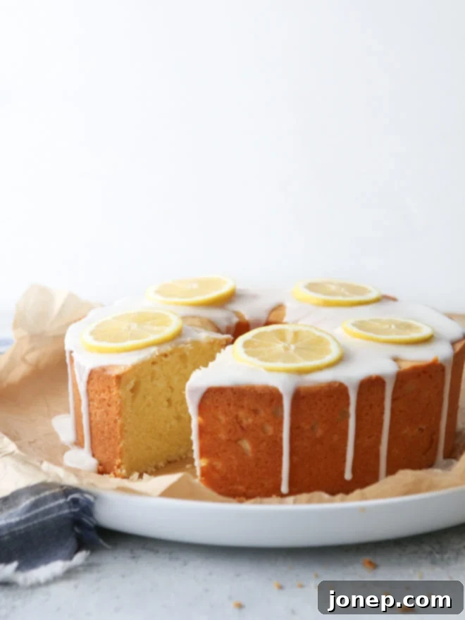A beautifully sliced Lemon Cream Cheese Pound Cake with a golden crust and luscious white lemon glaze, showcasing its moist interior, garnished with fresh lemon slices.