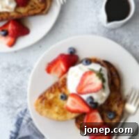 Ultimate French Toast 5 A stack of golden brown French toast slices with warm maple syrup and fresh berries, beautifully presented and ready to be served for a delightful breakfast.