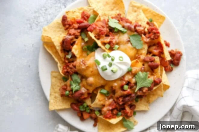 Ultimate Chili Cheese Nachos 3 Overhead view of a plate piled high with golden tortilla chips, rich chili, and melted cheese