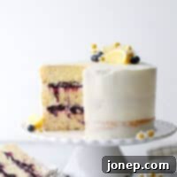 A beautifully decorated lemon butter cake with fresh blueberries and lemon zest, featuring layers of tender cake and sweet blueberry preserves, frosted with silky lemon buttercream.