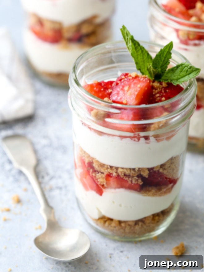 Layers of fresh strawberries, creamy yogurt whipped cream, and crunchy graham cracker crumble make up these adorable and irresistible parfaits, served in glass jars.