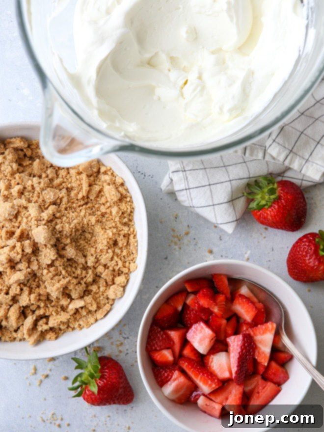 Close-up of a strawberry yogurt parfait, showing distinct layers of red strawberries, white whipped cream, and golden brown graham cracker crumble.