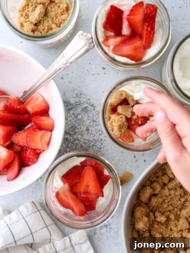A hand holding a spoon, scooping into a strawberry yogurt parfait, showcasing the delightful layers and textures.